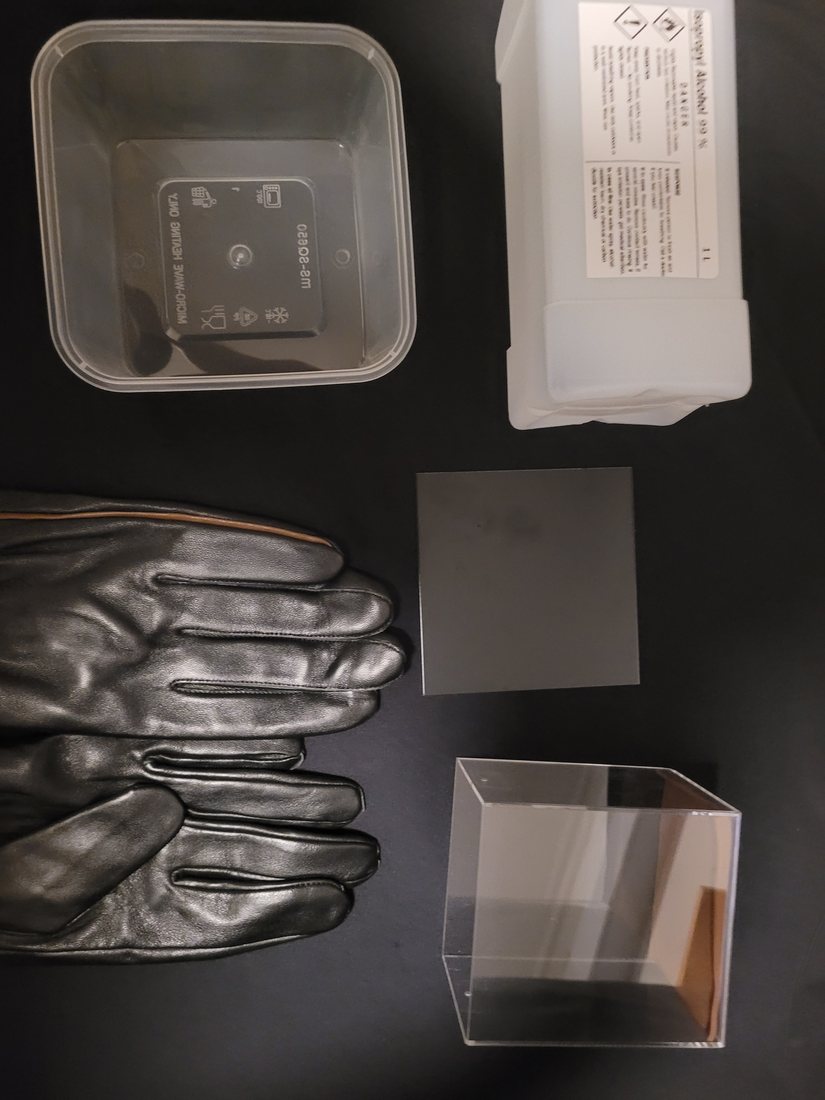 Overhead view of the chamber components laid out: sealed acrylic box, torch, isopropanol bottle, black plate and container.