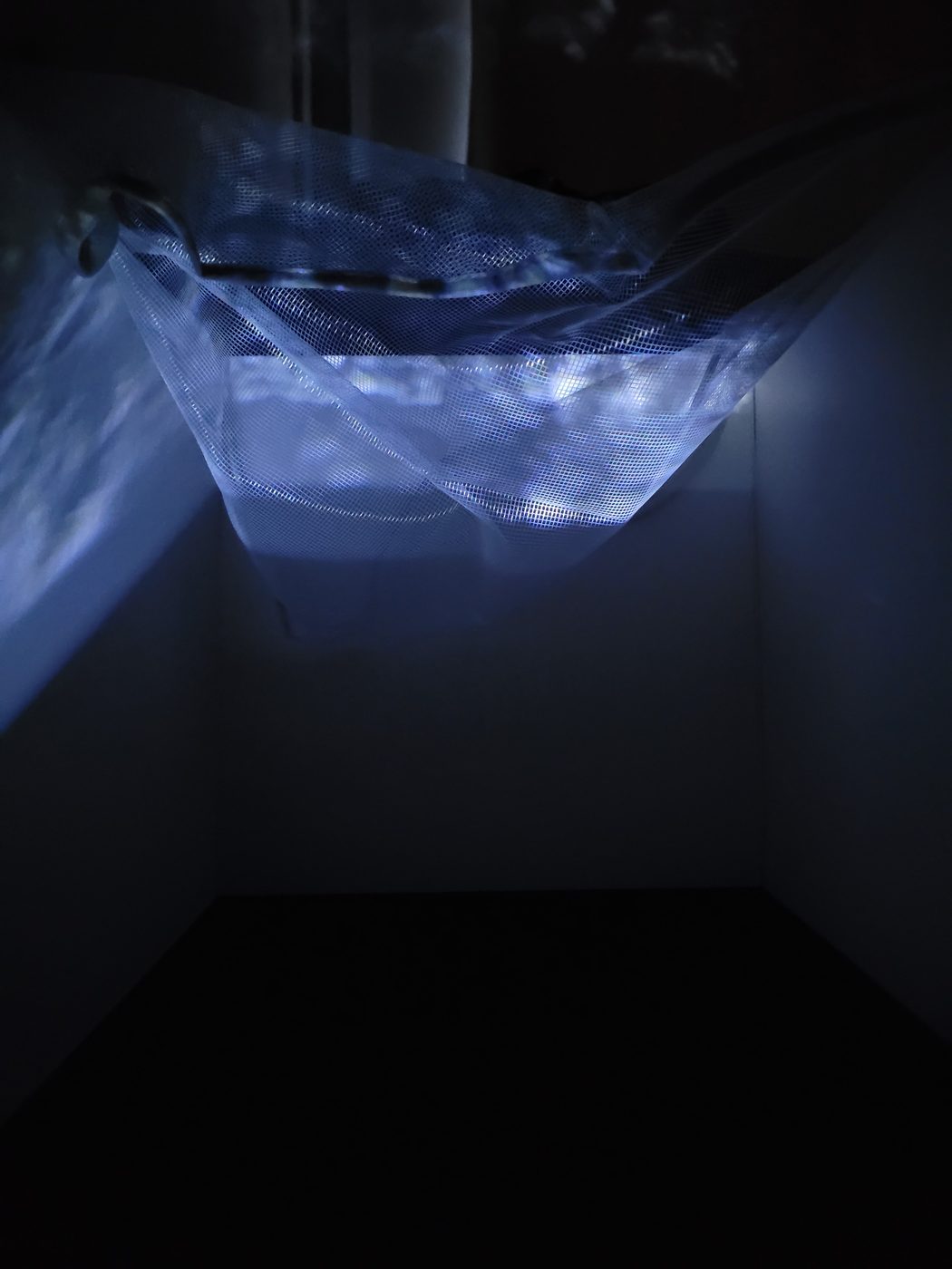 The same model from a lower angle: light from the projection passes through the mesh and falls softly on the wall and floor behind it.