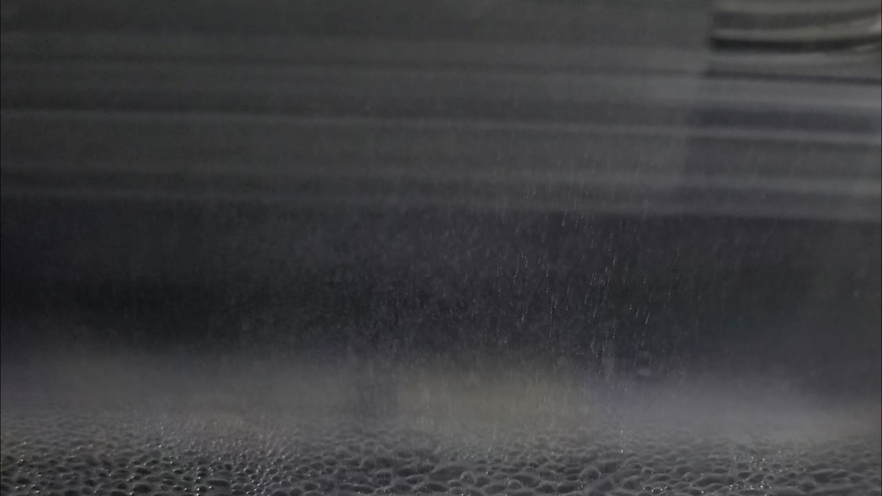 Raw chamber frame: grey fog, horizontal glare bands, streaks of falling alcohol and a bubbly condensation carpet along the bottom.