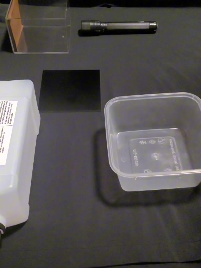 Overhead view of the chamber components laid out: sealed acrylic box, torch, isopropanol bottle, black plate and container.